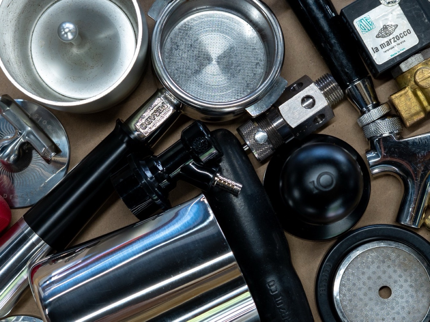 Espresso machine parts laid out, portafilters, shower screens, baskets, steam tips, gaskets, and a La Marzocco solenoid